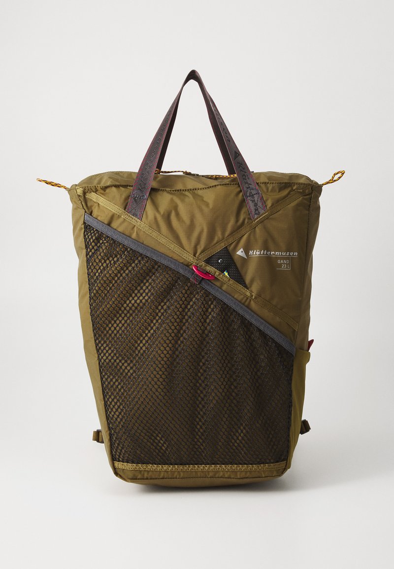 Zaino verde oliva con un pannello in rete, accenti in pelle e spallacci a contrasto. Presenta una tasca con cerniera e un'apertura superiore regolabile con cordoncino.