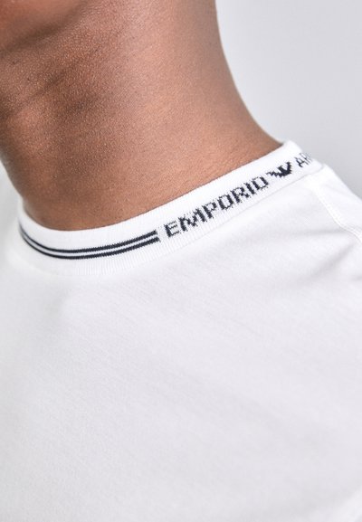 Valkoinen puuvillainen t-paita, jossa on ribbauskaulus ja mustavalkoinen "Emporio" -brändäys sekä raidallinen yksityiskohta. Sujuva rakenne.