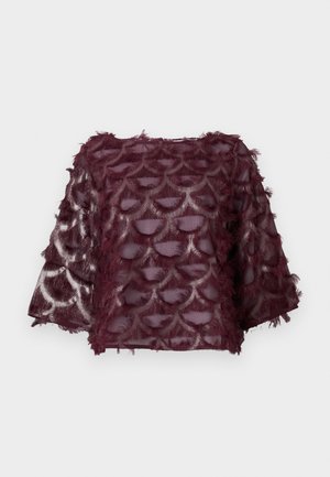 Burgunderbluse med et gennemsigtigt stof med en bølget mønster og frynse detaljer. Boxy form med brede ærmer. Teksturmønstre.