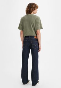 Green cotton t-shirt with short sleeves, paired with dark blue flared denim jeans featuring rear pockets and stitching accents.
