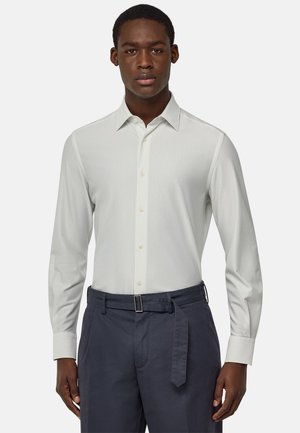 Camisa de manga larga a rayas gris claro con cuello abotonado, con textura suave y un corte entallado, combinada con pantalones oscuros.