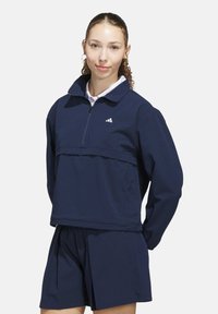 Navy blue sports jacket with a quarter-zip, ribbed texture, and logo accent. Paired with matching shorts, both designed for active wear.