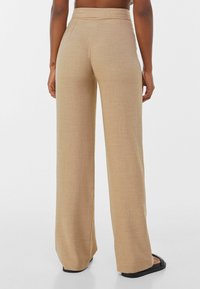 Beige, weitgeschnittene Hose aus strukturiertem Stoff mit glatter Oberfläche und hochgeschnittenem Design; verfügt über versteckte Taschen und einen sauberen Saum.