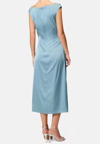 Abito lungo in satin blu con una silhouette aderente, maniche a cappuccio e una sottile cerniera sul retro. Abbinato a sandali con tacco a spillo.