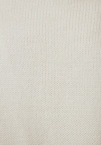 Tessuto lavorato a maglia di un morbido colore crema, con una trama uniforme e un motivo di punto intrecciato, che conferisce un aspetto lineare e sottile.