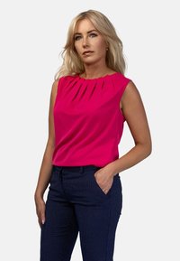 Fuksjowy bezrękawnik z plisowanym dekoltem, zestawiony z granatowymi spodniami w kropki. Gładki materiał i dopasowany fason.