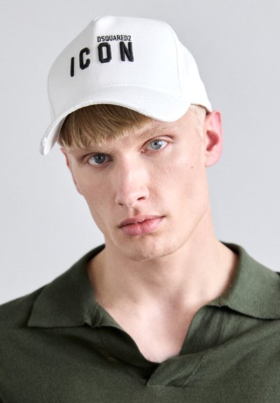 Weißer Baseballcap mit schwarzem "ICON"-Text und strukturiertem Schirm. Das Model trägt ein dunkelgrünes Poloshirt. Glatte Stoffoberfläche.