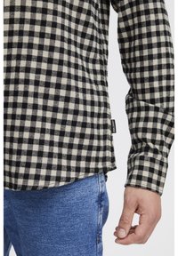 C�ămașă din flanel în carouri alb-negru, cu mâneci lungi, având un tiv curbat și un material texturat. Asortată cu blugi de denim de un albastru deschis.