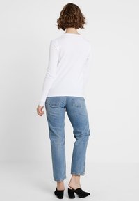 Bílý svetr, modré džíny a černé lodičky. Svetr má přiléhavý střih; džíny jsou volného střihu, mírně ohrnuté na kotnících.