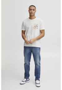 Kortærmet hvid bomulds t-shirt med en farverig mønstret lomme, parret med lyseblå denim jeans og sort-hvide sneakers.