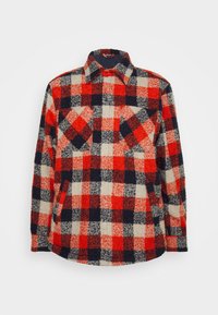 Camisa de flanela xadrez em vermelho, azul-marinho e creme, com colarinho clássico, dois bolsos no peito e fecho de botão. Tecido texturizado, aparência quente.