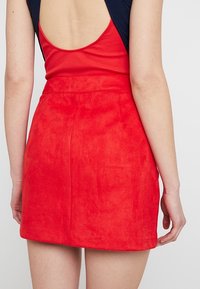 Mini-jupe en daim rouge à la texture lisse, avec une taille cintrée et une coupe droite. Le design arrière est simple, sans fermetures visibles.