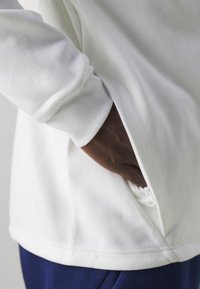 Witte sweatshirt met een geribde manchette en zijzak, voorzien van een subtiele ritsdetail. Zachte stof en een ontspannen pasvorm.