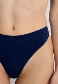 Tumman sininen kammattua bikini-alushousua, jossa on korkeavyötäröinen muotoilu. Materiaalissa on sileä rakenne ja minimaalinen ommel, mikä korostaa hoikkaa siluettia.