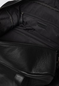 Black leather bag interior featuring a large compartment, a zippered pocket, and a soft fabric lining with a label tag visible.