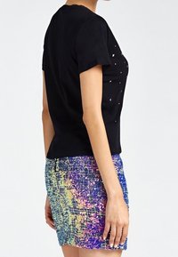Camiseta negra de manga corta con pequeños adornos blancos combinada con una mini falda texturizada multicolor que presenta un patrón degradado.