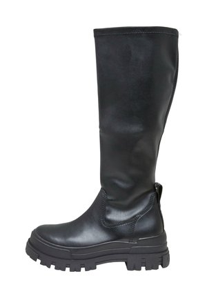 Persona que lleva botas negras hasta la rodilla y una minifalda rosa, de pie en una acera de la ciudad bajo la luz del sol.