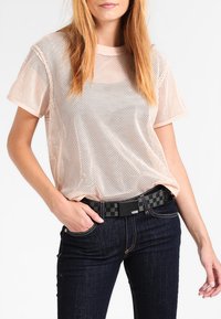 Mesh T-shirt met korte mouwen in lichtroze, met een losse pasvorm en een gemêleerd patroon; gecombineerd met donkere spijkerbroek en een zwart geruit riem.