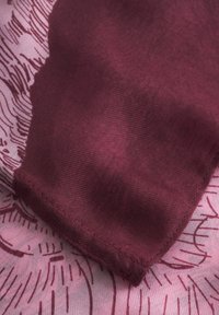 Tissu bordeaux avec une texture lisse, bords cousus, sur un fond rose comportant un motif imprimé subtil.