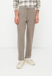 Beige, lichtgewicht sweatpants met een elastische tailleband en een trekkoord. Tapered vorm en zachte textuur, gecombineerd met witte sneakers.