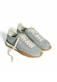 Baskets gris clair présentant un mélange de suède et de matière lisse, une semelle blanche, des lacets ronds et une bande d'accent verte sur le talon.