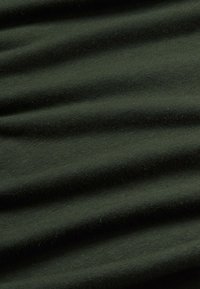 Tissu en coton extensible vert foncé avec une texture lisse et des ondulations subtiles, mettant en valeur sa nature flexible et douce.