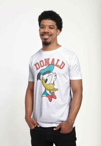 Biała bawełniana koszulka z kolorową grafiką Kaczora Donalda, z czerwoną napisą "DONALD" powyżej i niebieskim detalem czapki.