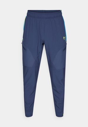 Navy athletic pants with an elastic waistband, tapered legs, side zippers, and green accents on pockets and logo. Lightweight, smooth fabric.