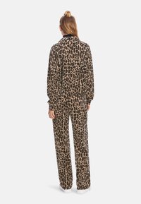 Dres w panterkę w odcieniach beżu i czerni. Posiada zapinaną na zamek bluzę z długimi rękawami oraz pasujące luźne spodnie. Gładka tekstura.