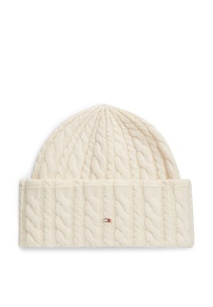 Kremowa dziergana czapka typu beanie z szerokim złożonym mankietem i małym prostokątnym logo w kolorach czerwonym, białym i niebieskim z przodu.
