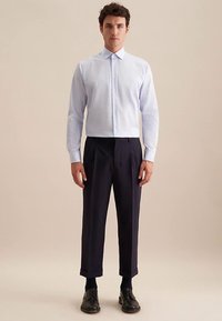 Camicia a righe azzurro chiaro con colletto a punta, abbinata a pantaloni blu scuro. Scarpe eleganti nere completano l'outfit.