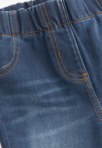 Denim bleu foncé avec une texture douce, doté d'une taille élastique et de coutures orange. Comprend des détails de poches avant et arrière.