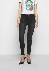 Black skinny jeans with a mid-rise waist, paired with a white graphic t-shirt featuring colorful floral and figure designs. High-heeled black shoes.
