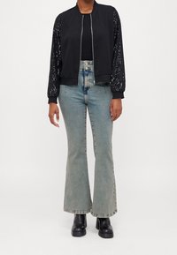 Czarna kurtka typu bomber z rękawami ozdobionymi cekinami, skomponowana z jasnoniebieskimi dzwonami i czarnymi botkami na obcasie. Prosty krój i teksturowane akcenty.