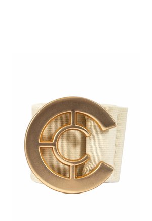 Cinturón de tela beige con una gran hebilla redonda metálica dorada con un diseño recortado de formas concéntricas de la letra C.