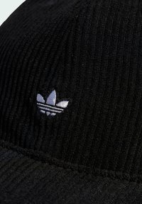 Čierna kordurová čiapka s textúrovaným rebrovaním. Na prednej strane má malé biele vyšívané logo Adidas trefoil.
