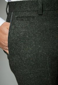 Dunkle, strukturierte Hose aus Wollmischung. Verfügt über eine Seitentasche und dezente Farbkleckse im Stoff. Maßgeschneiderte Passform.