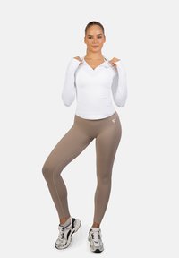 Bela dolga majica z dolgimi rokavi in zadrgo ter prilagojene bež legice, ki so kombinirane z masivnimi belimi in črnimi supergami. Gladek material, športni kroj.