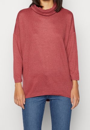 T-shirt surdimensionné à manches longues dans une douce teinte rose texturée, avec un col montant et un ourlet légèrement arrondi. Associé à un jean en denim bleu.