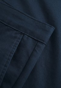 Navy blue fabric with a smooth texture, featuring folded layers and visible stitching details. The material appears sturdy and structured.