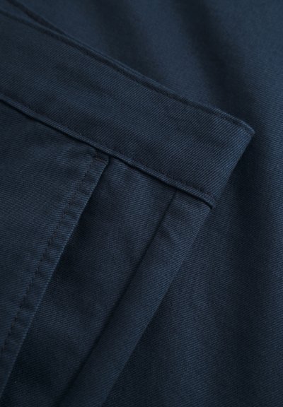 Tissu bleu marine au toucher lisse, présentant des couches pliées et des détails de couture visibles. Le matériau semble solide et structuré.