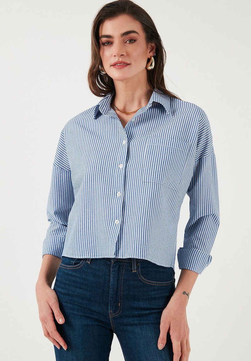Blue and white striped button-up shirt with a collar, long sleeves rolled at the cuffs, and a chest pocket. Made from a lightweight fabric.