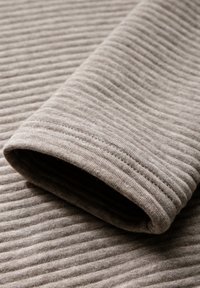 Vaalea ruskea ribattua kangasta pehmeällä pinnalla. Kääritty hihansuu näyttää kapeita pystysuoria raitoja, luoden hienovaraisen kuvion.