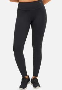 Leggings negros con una cintura alta, hechos de un material elástico que se ajusta a las piernas hasta los tobillos; cuentan con una textura suave y mate.