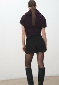 Jersey de manga corta burdeos superpuesto sobre una falda mini negra ajustada, combinado con botas altas negras y medias negras transparentes.