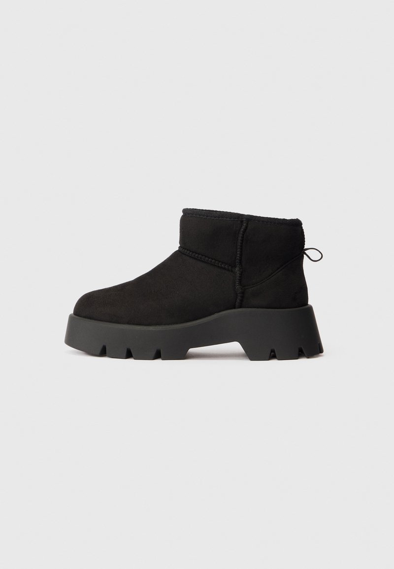 Botas de camurça pretas até ao tornozelo com uma sola plataforma cinza robusta. Apresentam um bico arredondado e detalhes de costura mínimos. Altura curta com uma alça para puxar.