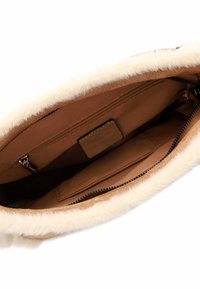 Interno di una borsa in suede marrone con rifinitura in pelliccia sintetica crema. Presenta una tasca con zip e una tasca a flap, con una foderatura in tessuto liscio.