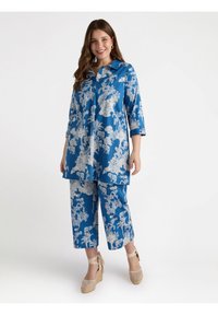 Niebieski zestaw tuniki i spodni z białymi kwiatowymi i zwierzęcymi wzorami. Tunika ma kołnierzyk i rękawy o długości trzech ćwierci; spodnie są krótkie.