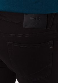 Jeans in denim nero con un patch in pelle Hi-Flex, caratterizzati da dettagli di cucitura sottili e un design standard della tasca posteriore.