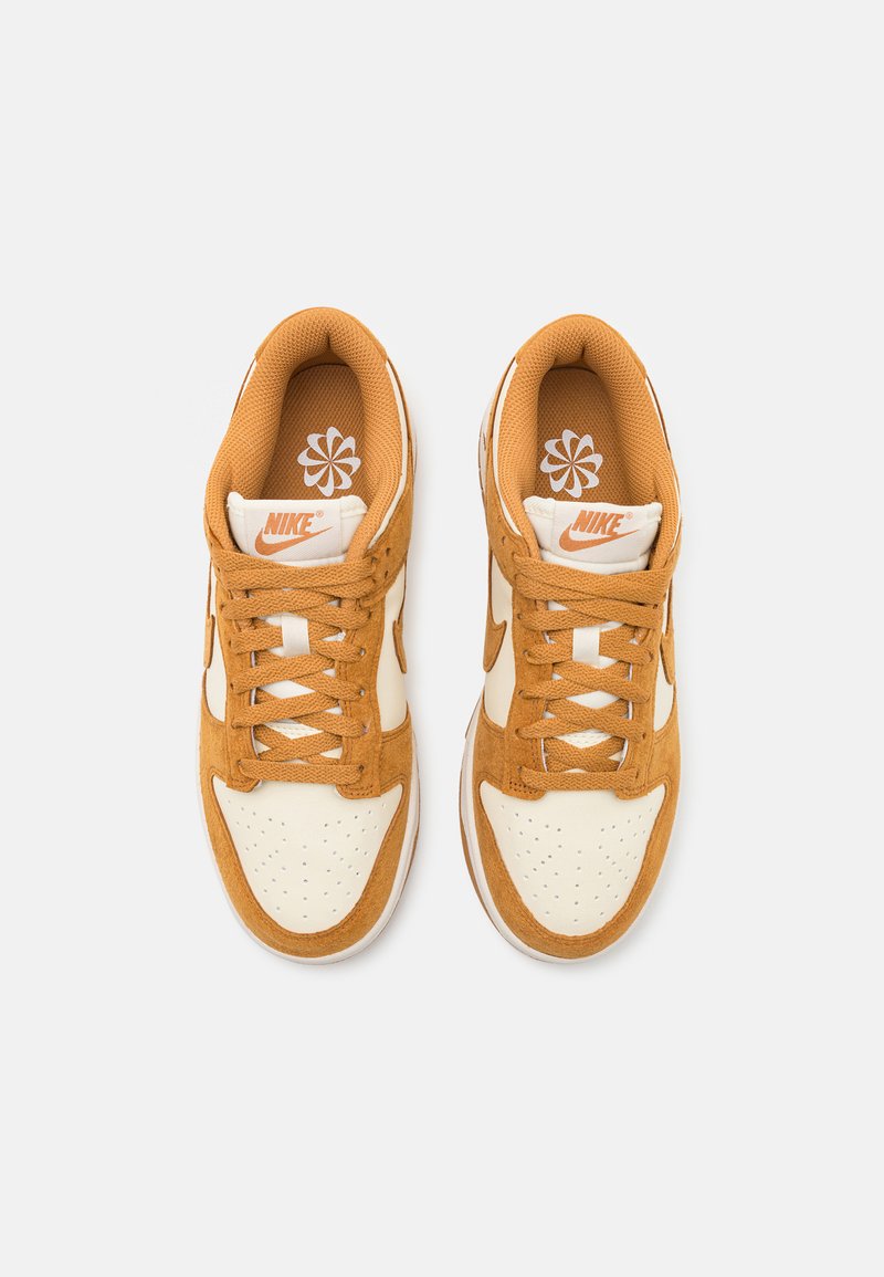 Baskets Nike présentant une combinaison de couleurs beige et crème, en matériaux suede et mesh, avec des lacets ronds, une boîte à orteils perforée et des accents de marque.